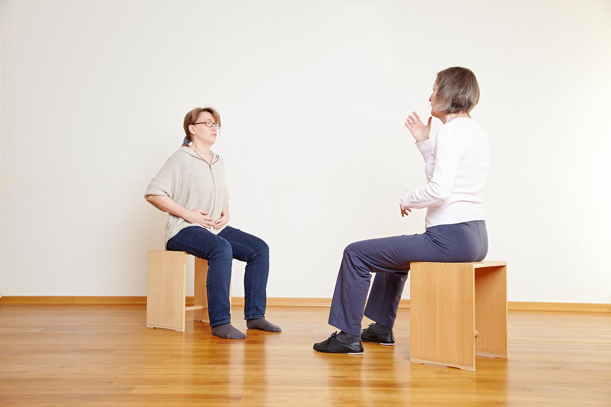 Zwei Frauen sitzen auf Holztaburetten und besprechen eine Atemübung.