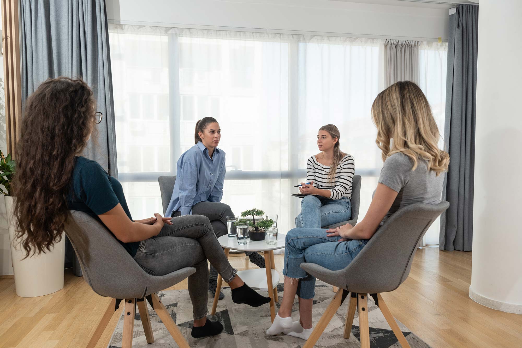 Vier junge Frauen sitzen in Kreis um einen Tisch und halten eine Besprechung ab.
