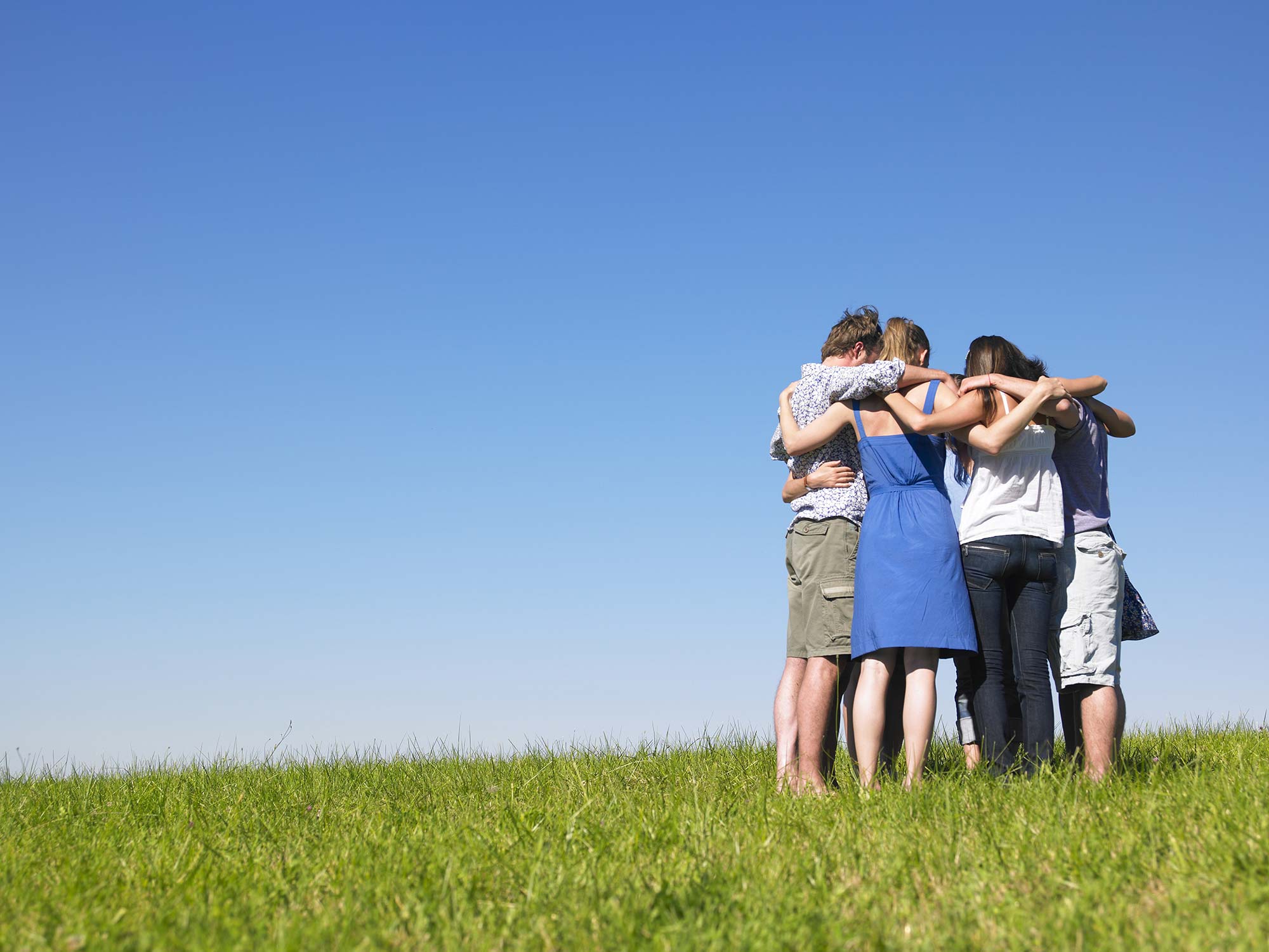 Sechs Personen stehen in einem engen Kreis und halten einander an den Schultern.
