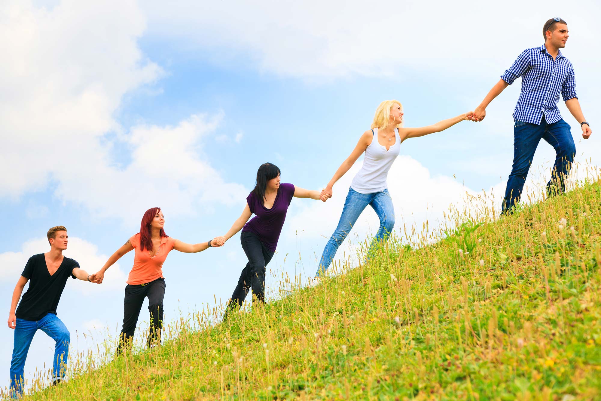 Fünf junge Personen halten einander an den Händen und steigen einen Hügel hinauf.