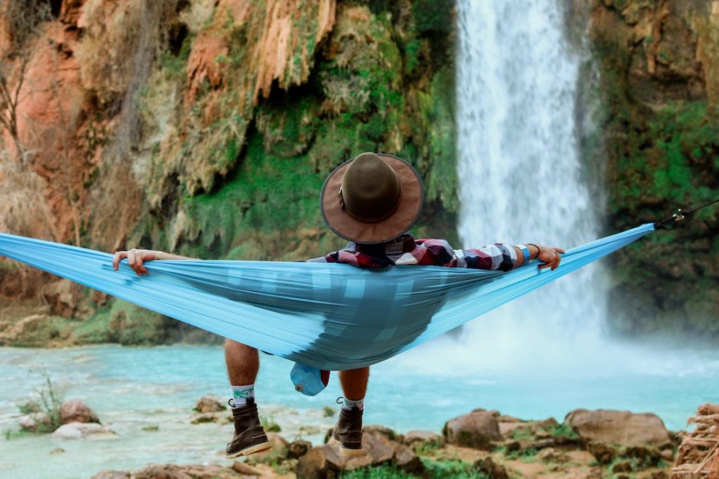 Ein Mann liegt vor einem Wasserfall in einer Hängematte.